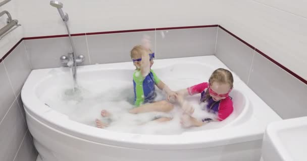 Niños en gafas de baño azules y rosadas lanzándose una espuma entre sí . — Vídeo de stock