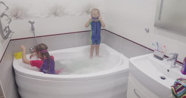 Kleiner Junge setzt blaue Schwimmbrille auf und springt in Badewanne ins Wasser. — Stockvideo