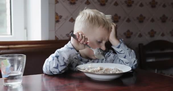 Nachdenkliches Kind beim Frühstück beim Zeichentrickgucken auf dem Handy. — Stockvideo