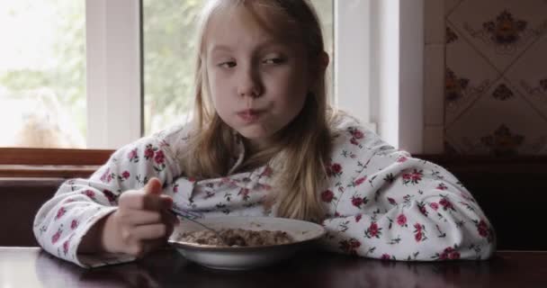 Närbild av barn flicka ansikte medan hon äter gröt. — Stockvideo