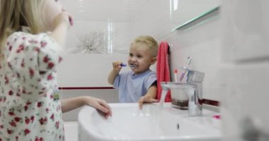 Pijamalı bir erkek ve kız kardeş banyo aynasının önünde dişlerini fırçalıyorlar..