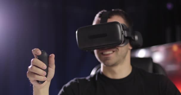 Человек в черной одежде смотрит через очки виртуальной реальности в наушниках с помощью пульта дистанционного управления . — стоковое видео