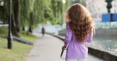 Happy girl with bright red hair is walking in summer park with cotton candy during sunset.