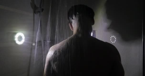 Sportsman is taking a shower in a dark room. — Stockvideo