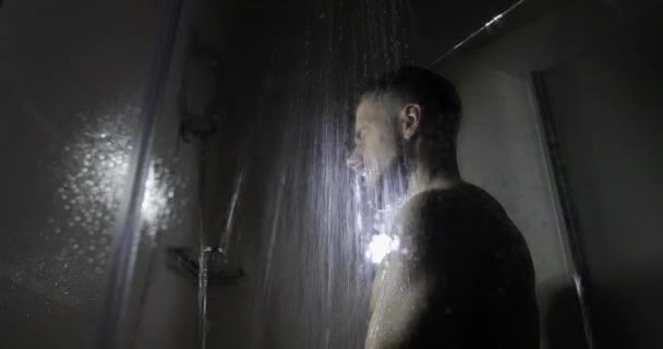 Un sportif musclé prend une douche dans une pièce sombre . — Video