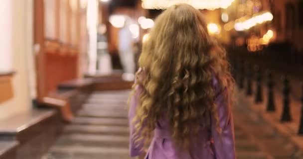 Mujer joven con el pelo rizado rojo caminando en la ciudad de la noche . — Vídeo de stock