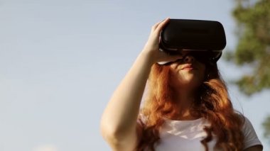 VR gözlüklü, kulaklıklı, çilli kızıl saçlı kız mavi gökyüzünün arka planında dönüyor..