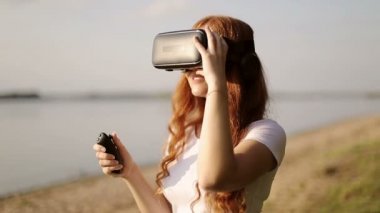 VR gözlüklü kızıl saçlı kız uzaktan kumandayla 360 derecelik video izliyor..