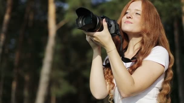Zonovergoten roodharig meisje met fotocamera lacht en kijkt naar de zonsondergang. — Stockvideo