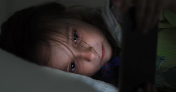 女の子はベッドに横になり、自宅で夕方には携帯電話を見て. — ストック動画