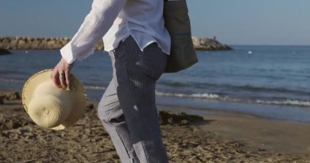 Närbild händer av en gammal kvinna som håller i en hatt och går på stranden. — Stockvideo