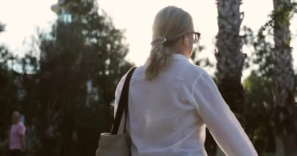 Gammal kvinna i hörlurar går utomhus på en solnedgång bakgrund. — Stockvideo