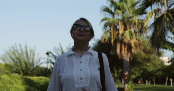 Une vieille femme avec des rides profondes dans les lunettes de soleil marche. — Video