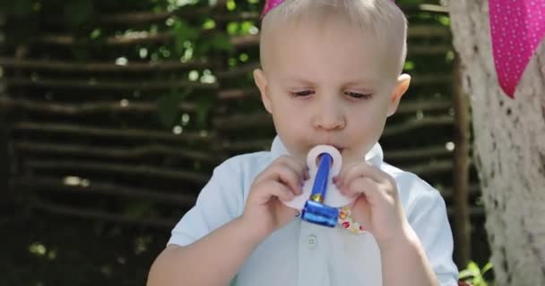 Feliz niño está soplando en el tubo desplegable en una fiesta de cumpleaños. — Vídeos de Stock