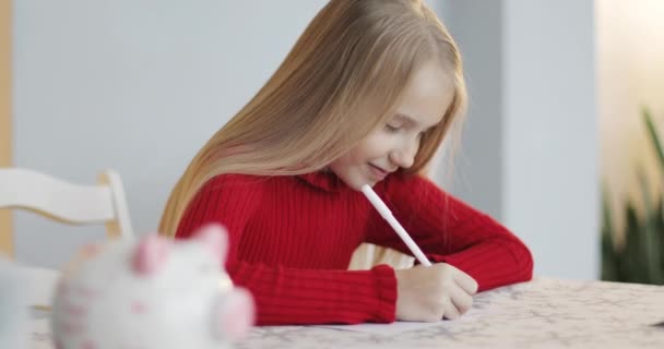 En skolflicka med blont hår i en röd tröja håller en penna i händerna. — Stockvideo