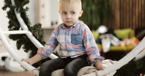 Cute boy is riding on a Christmas swing in the studio. — Stock Video