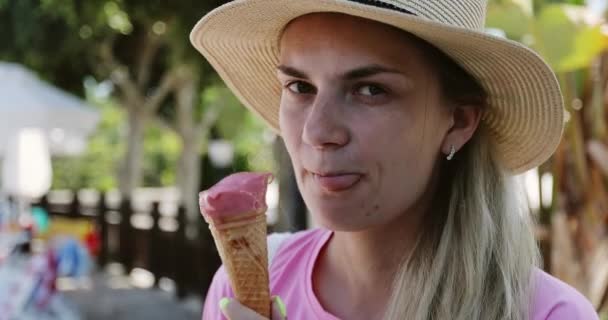 Mujer en un sombrero come helado rosa en un cono de vacaciones. — Vídeo de stock