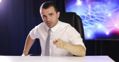 Bir iş adamı kameraya konuşur ve işaret parmağını sallar..