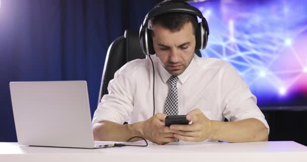 Junger Büroleiter tippt über Kopfhörer eine Nachricht auf sein Handy. — Stockvideo