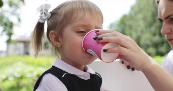Mère aide une petite fille à boire avec un verre de vacances en papier. — Video