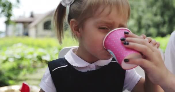 Mamma aiuta una bambina a bere da un bicchiere all'aperto. — Video Stock