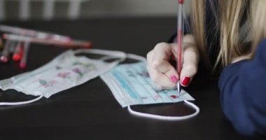 Tıbbi bir maskenin üzerine kalp çizen kızın elleri..