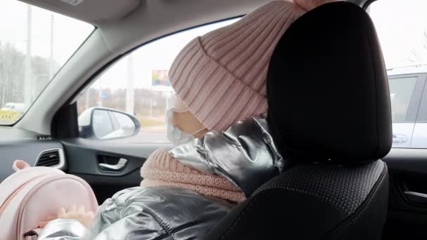 Close-up gezicht van een schattig klein meisje in een winter hoed masker rijdt in een auto. — Stockvideo