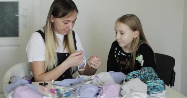 Una joven madre viste a su hija con una máscara médica cosida. — Vídeo de stock