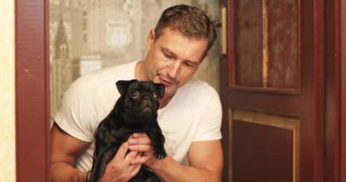 Bir adam kollarında siyah bir köpek tutuyor.. 