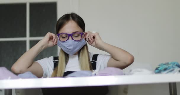 Gözlüklü genç bir kadın el yapımı tıbbi maskeler dikiyor.. — Stok video