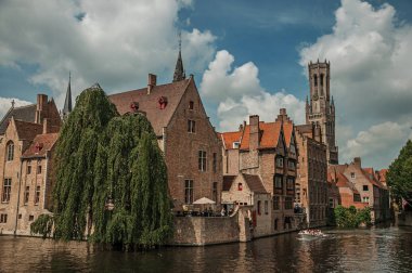 Bruges kanalı üzerinde tuğla binalar ile tekneler ve yapraklı ağaç