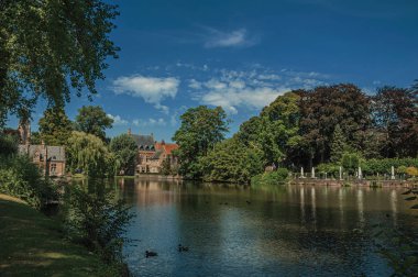 Bruges'te yeşillikler ve eski tuğla binaile çevrili göl