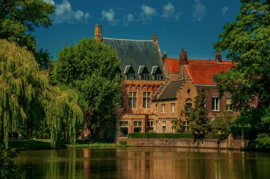 Bruges'te yeşillikler ve eski tuğla binaile çevrili göl