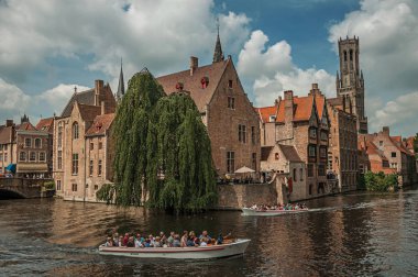 Bruges kanalı üzerinde tuğla binalar ile tekneler ve yapraklı ağaç