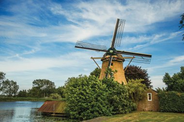 Geniş nehrin yanındaki ahşap yel değirmeni ve Weesp 'teki yapraklı çalılar.