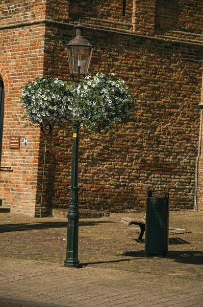 Flowers on public lamp post and wall made of bricks in Weesp