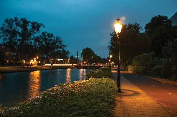 Night view of wide canal with bridge and lamp post in Weesp