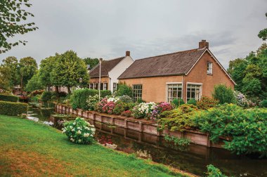 Canal next to rustic houses with flowery garden in Drimmelen