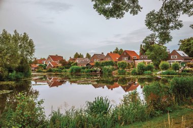 Canal next to rustic houses with bushes and trees in Drimmelen