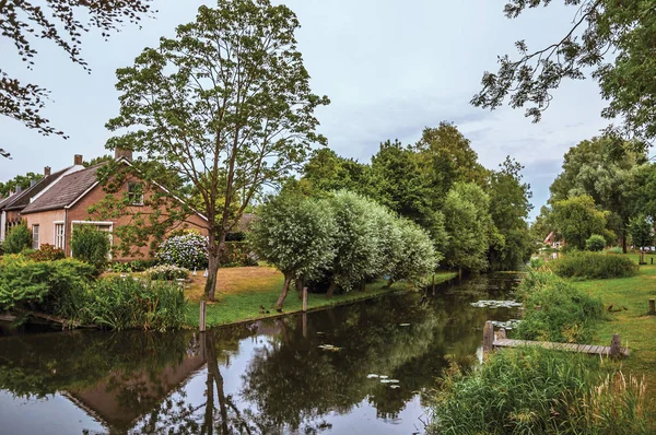 Canal next to rustic house with garden and trees in Drimmelen