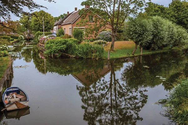 Canal next to rustic house with garden and trees in Drimmelen