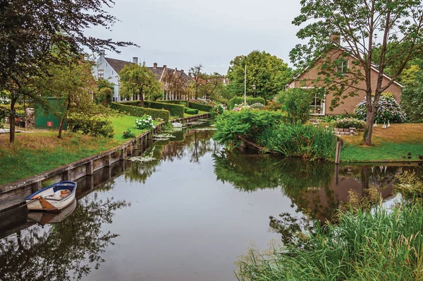 Canal next to rustic houses with garden and trees in Drimmelen