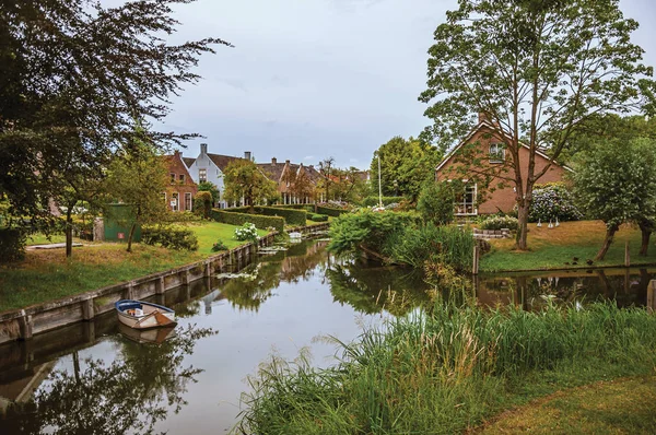 Canal next to rustic houses with gardens and trees in Drimmelen
