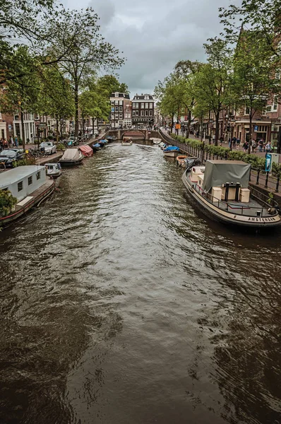 Gracht met bakstenen gebouwen en afgemeerde boten in Amsterdam — Stockfoto