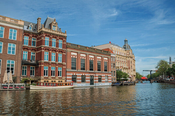 Canal with old brick buildings and moored boats in Amsterdam