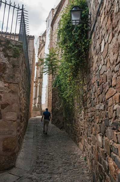 Cobblestone alley amidst stone old buildings with a man walking at Caceres