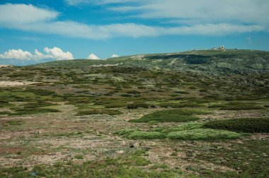 Çalılar ve eski bir radar istasyonunun kubbeleri ile kayalık manzara
