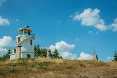 Çimen ve ağaçlarla kaplı tepenin tepesindeki deniz feneri