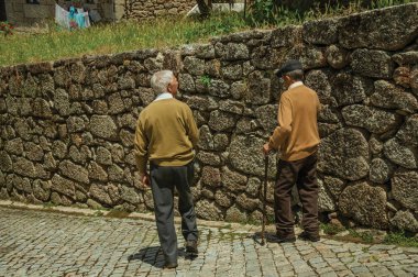 Taş duvarın yanındaki yamaçta sokakta yürüyen yaşlı insanlar