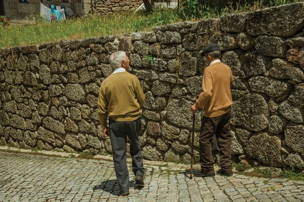 Old people walking down the alley on slope next to stone wall — Stock Photo, Image